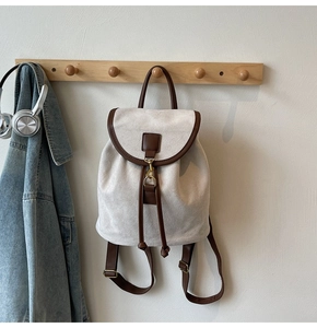 Detail of drawstring flap backpack in cream canvas with brown leather trim and gold hardware