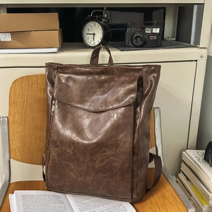 Sac à dos vintage en similicuir marron foncé avec rabat sur une chaise