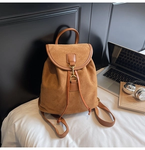 Detailed close-up of brown suede backpack showing the flap and metallic buckle closure