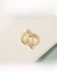 Détail du logo en métal doré sur le sac en cuir grainé blanc et vert pastel