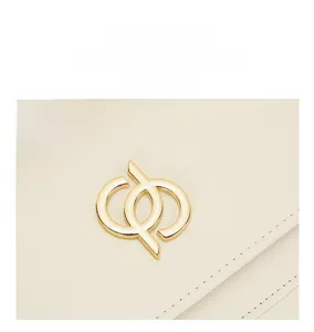 Détail du logo en métal doré et de la bandoulière sur le sac à bandoulière en cuir crème
