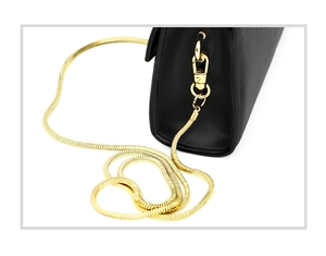 Macro detail of high-gloss gold snake chain and lobster clasp on black leather phone bag