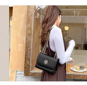 Détail d'un sac bandoulière en cuir noir avec logo doré entrelacé et fine chaîne dorée