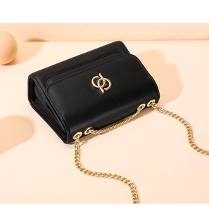 Détail d'un sac à bandoulière noir avec logo métallique doré et chaîne sur support élégant