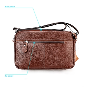 Detailed macro view of brown lychee grain leather crossbody bag with functional zip pockets