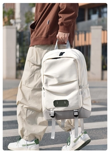 Cream white travel backpack with grey base and green patch shown in city street