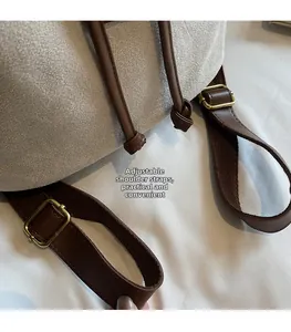 Detail of adjustable brown leather shoulder strap with gold hardware on gray suede backpack