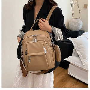 Close-up of khaki faux leather backpack featuring multiple zip pockets and a small coin purse