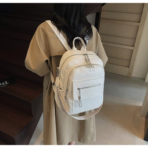 Detail of white litchi pattern backpack with woven strap and silver chain accessory