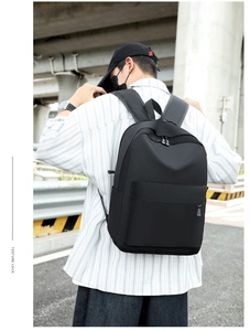 Outdoor street view of a minimalist black oxford backpack with front zipper pocket
