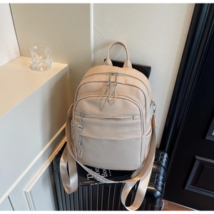 Beiger Lederrucksack mit Reißverschlusstaschen und breiten Riemen auf einem Koffer