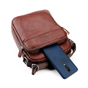Détail du sac bandoulière en cuir montrant le compartiment principal avec un téléphone