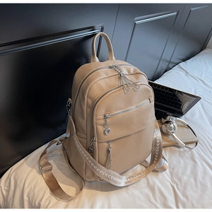 Detail eines beigen Lederrucksacks mit Jacquard-Riemen und silbernem Kettenanhänger