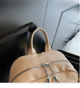 Detail of beige lychee leather backpack showing sturdy handle and dual metal chain zippers