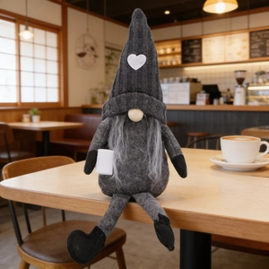 Detail of a knitted grey gnome doll with heart pattern sitting in a cozy coffee bar setting