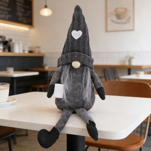 Detail of a handmade coffee gnome plush with a knit hat and white heart on a cafe table