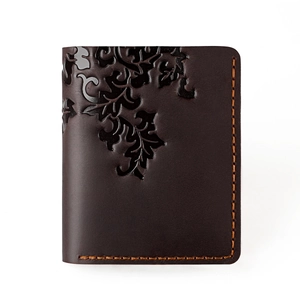 Detail of vintage brown leather wallet with embossed vine pattern and orange hand stitching