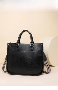 Détail du sac cabas en cuir grainé noir avec bandoulière rayée et boucles dorées