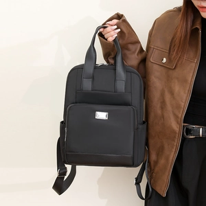 Détail d'un sac à dos en nylon noir avec poignées et poche zippée tenu par un mannequin