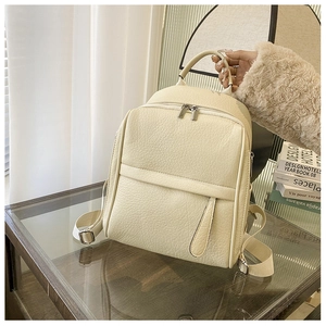 Détail du sac à dos en cuir PU crème avec texture litchi et fermeture éclair sur table en verre