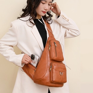 Detail view of multi-pocket brown leather sling bag with zippers worn by a model