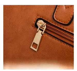 Détail macro du curseur de fermeture éclair en métal doré sur un sac en daim brun