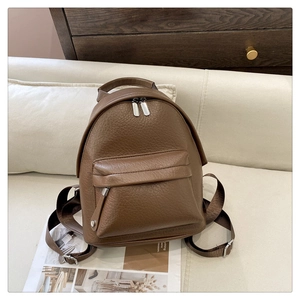Close-up of brown pebbled faux leather backpack with silver zippers on a beige sofa