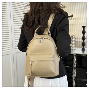 Close-up of beige faux leather backpack with textured pebble grain and silver zippers