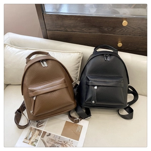 Detail of mini PU leather backpacks in brown and black on a sofa in a home setting