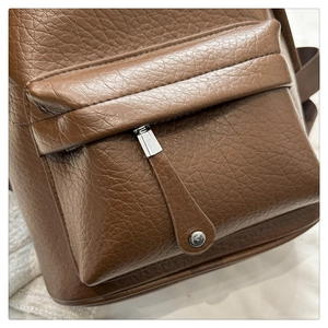 Detail of brown PU leather backpack featuring litchi texture and silver metal zipper pull