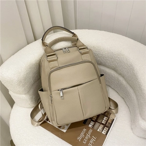Close-up of beige lychee grain PU leather backpack with silver zippers on a modern white sofa