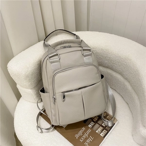 Detail of beige PU leather backpack with side pockets on a soft textured sofa