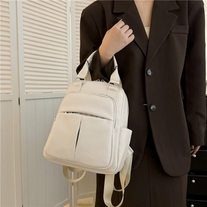 Detailed view of a white pebble leather backpack on a model in a brown blazer