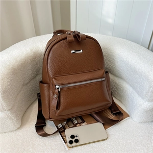 Detailed side view of brown lychee-textured PU leather backpack with silver metal logo plaque