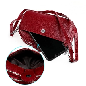 Détail du sac bandoulière en cuir rouge avec smartphone inséré dans la poche frontale