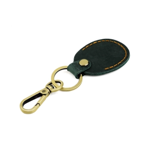 Detail of dark green leather AirTag holder with contrast stitching and brass hardware