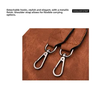 Close-up of detachable gun-black metal hooks and textured brown leather shoulder strap