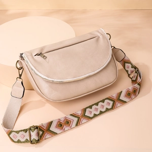 Close-up of beige crossbody saddle bag with vintage hardware and ethnic embroidery strap