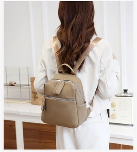 Close-up of khaki faux leather backpack featuring silver zippers and wide fabric straps