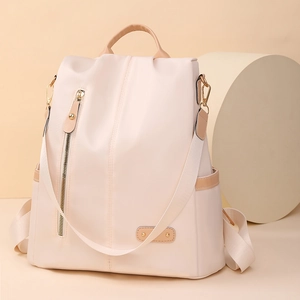 Detail of minimalist beige nylon backpack featuring golden zippers and side pocket storage