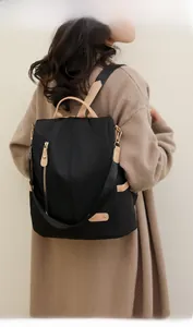Model wearing a large black nylon backpack with camel leather straps and gold hardware