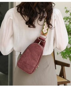 Deep red leather crossbody chest bag with colorful ethnic geometric woven strap on a model