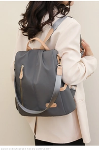 Detail of gray nylon backpack with brown leather trim shown on model in beige blazer