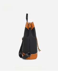 Side view of black Oxford fabric backpack with brown leather trim and drawstring detail