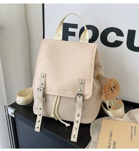 Detail of beige nylon backpack featuring leather straps and a brown plush charm on a rack