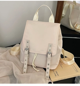 Detail of beige nylon backpack showing metal rivet straps and drawstring closure