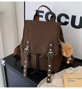 Detail of dark brown waterproof nylon backpack with rivets and plush ball charm