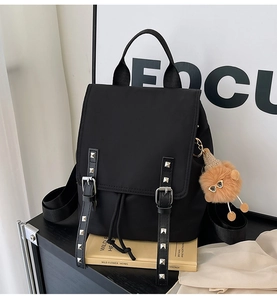 Detail of black nylon backpack with metal studs and cute brown bear pendant accessory
