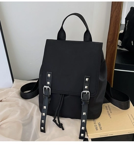 Detail of black nylon backpack featuring silver studs on leather straps and drawstring closure