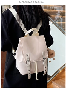 Close-up of cream backpack with silver studs and a brown plush bear on a model